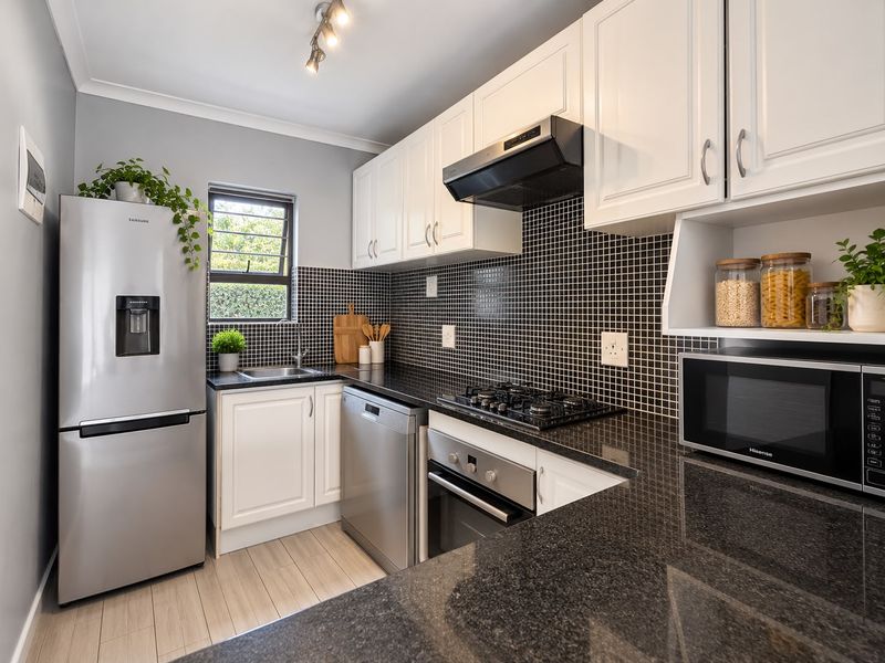 Modern kitchen featuring white cabinetry, black granite countertops, mosaic tile backsplash, and integrated stainless steel appliances including a gas hob and oven.
