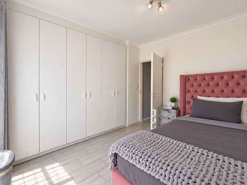A well-maintained bedroom featuring extensive floor-to-ceiling built-in cupboards, neutral tiled flooring, and modern finishes.