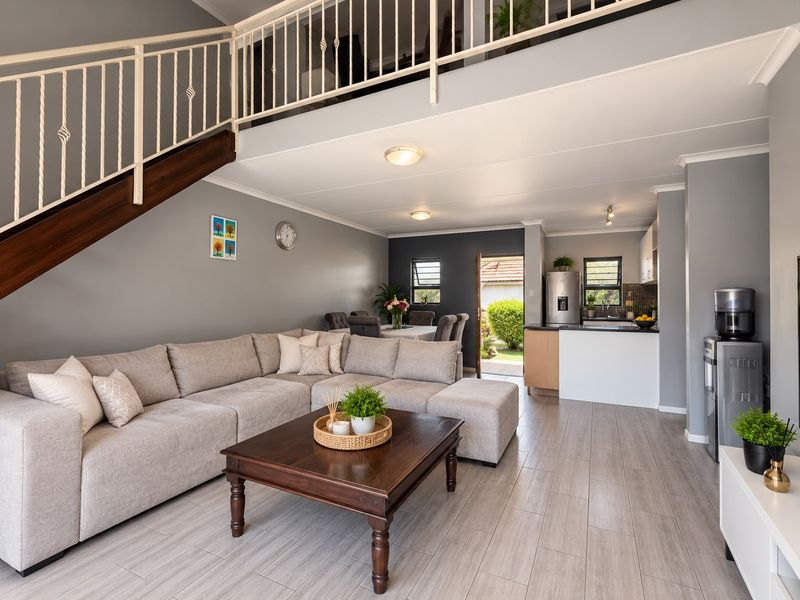 Spacious open-plan living area featuring a modern kitchen, tiled flooring, and a staircase with a metal balustrade leading to an upper level.