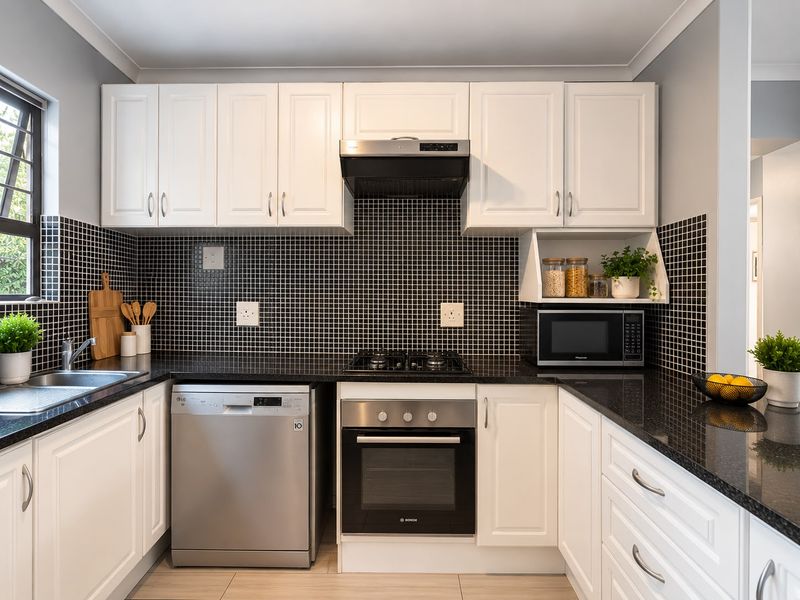 A well-maintained kitchen featuring white cabinetry, black granite countertops, a mosaic tile backsplash, and integrated stainless steel appliances.