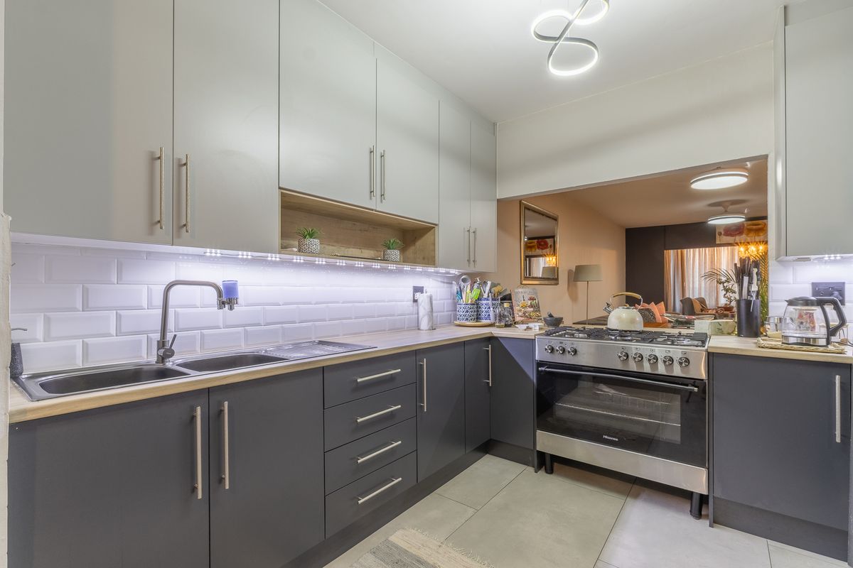 Modern kitchen featuring dark grey lower cabinetry, light grey upper cabinets, subway tile backsplash, and a stainless steel gas stove with oven.