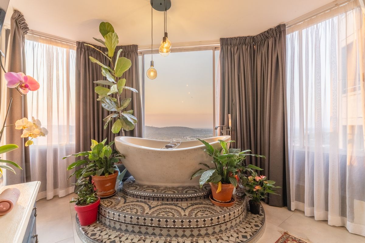 A luxurious bathroom featuring a raised tiled platform with a freestanding bathtub, positioned to enjoy panoramic views through floor-to-ceiling windows.