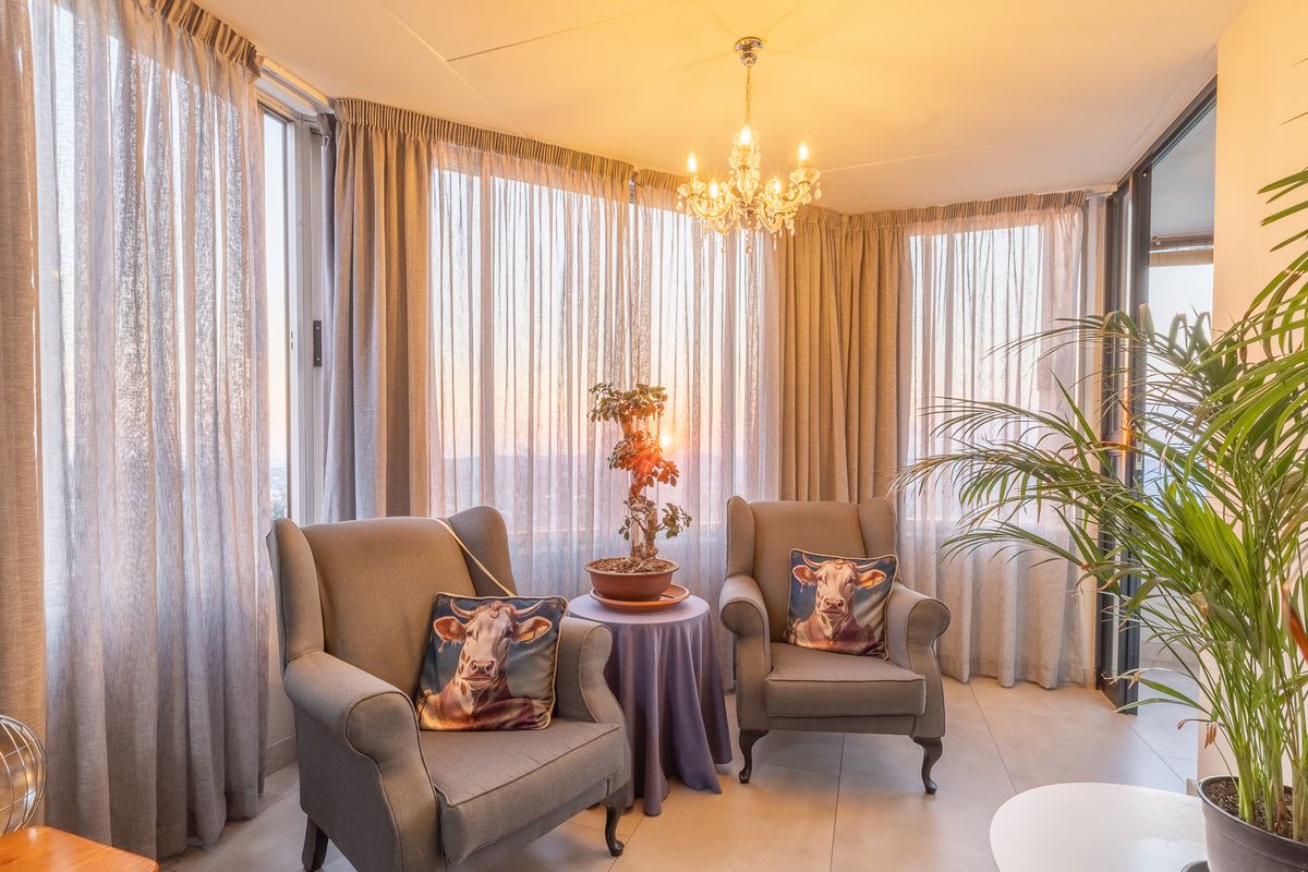 A bright living area featuring floor-to-ceiling windows with expansive views, elegant tiled flooring, and a classic crystal chandelier.