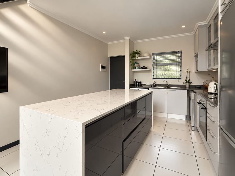 Modern kitchen featuring a large central island with quartz countertops, sleek cabinetry, built-in appliances, and high-quality tiled flooring.