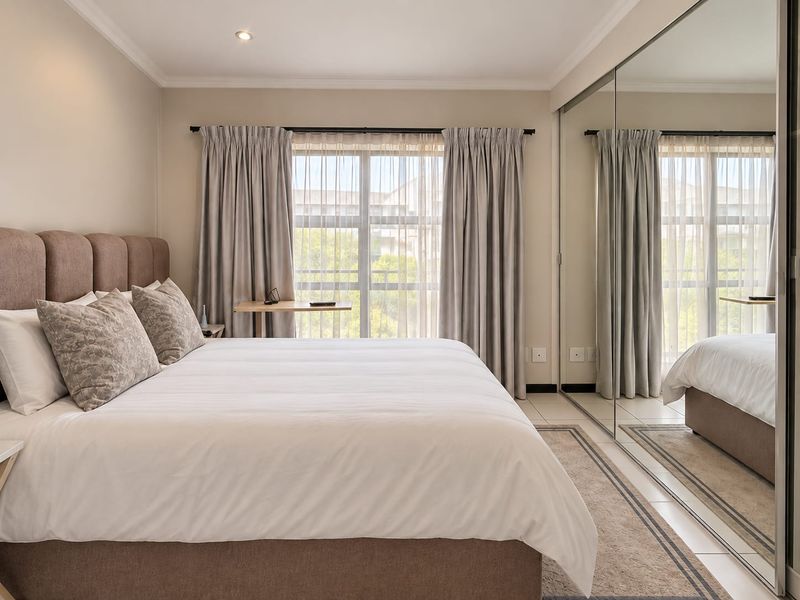 A well-maintained bedroom featuring tiled flooring, recessed lighting, and large mirrored sliding wardrobe doors that enhance the sense of space.
