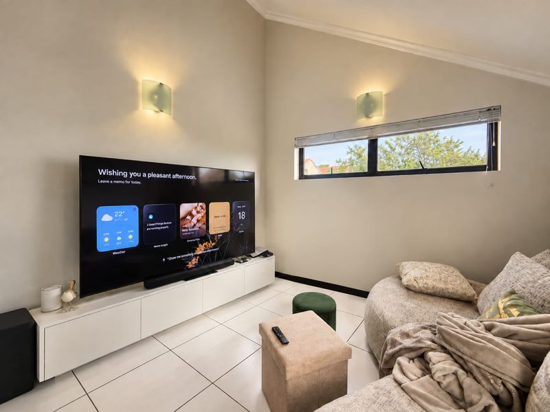 A bright living room featuring tiled flooring, a sloped ceiling, built-in media cabinetry, and a horizontal window providing natural light.