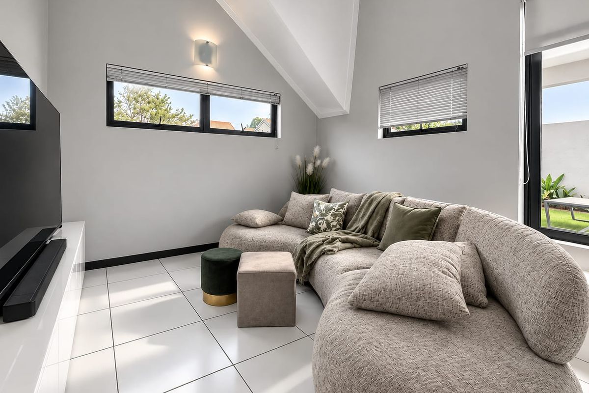Modern living room featuring vaulted ceilings, large black-framed windows, and sleek tiled flooring, creating a bright and contemporary atmosphere.