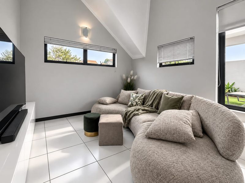 Modern living room featuring vaulted ceilings, large black-framed windows, and sleek tiled flooring, creating a bright and contemporary atmosphere.