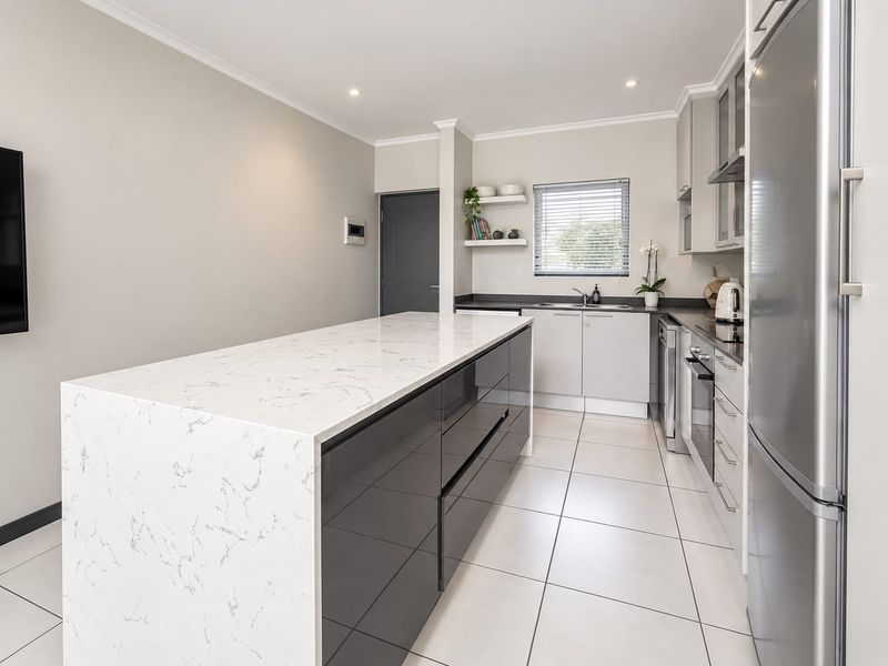 Modern kitchen featuring a large central island with quartz countertops, sleek cabinetry, built-in oven, and high-quality tiled flooring.