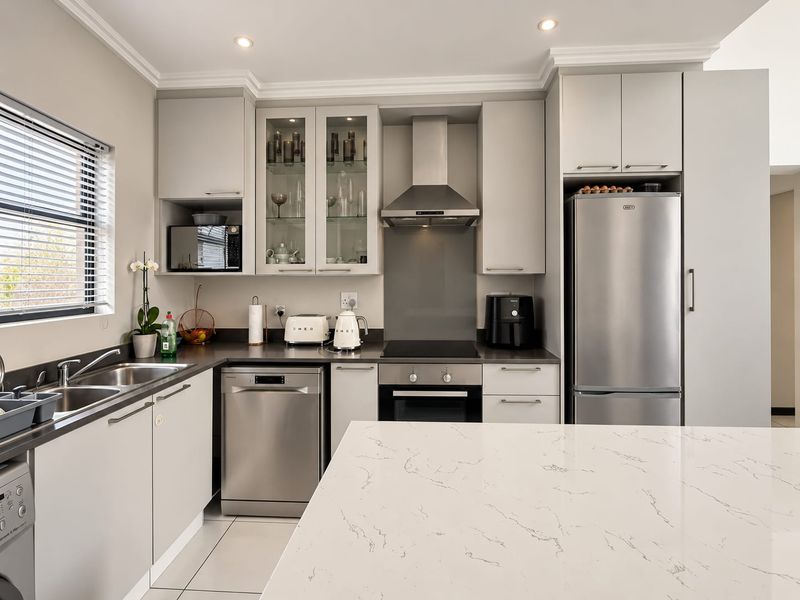 Modern kitchen featuring sleek light grey cabinetry, stone countertops, stainless steel appliances, and a functional layout with ample storage and recessed lighting.