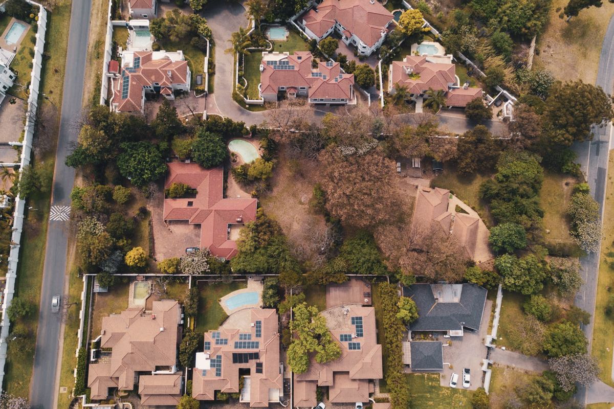 An aerial view of a residential neighborhood featuring multiple homes with tiled roofs, swimming pools, and established garden landscaping.