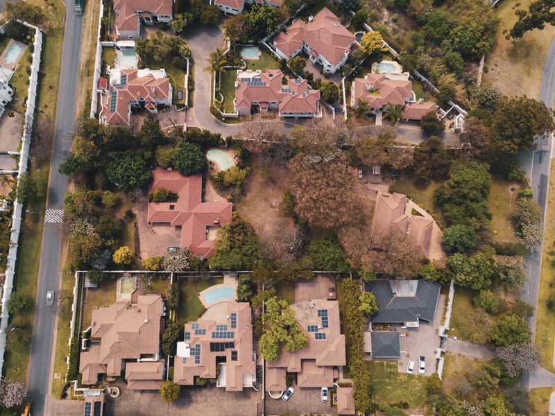 An aerial view of a residential neighborhood featuring multiple homes with tiled roofs, swimming pools, and established garden landscaping.