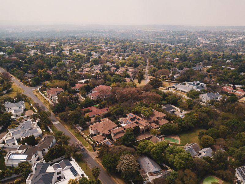 An elevated aerial view of a lush, established residential neighborhood featuring mature trees, paved streets, and various suburban homes with swimming pools.