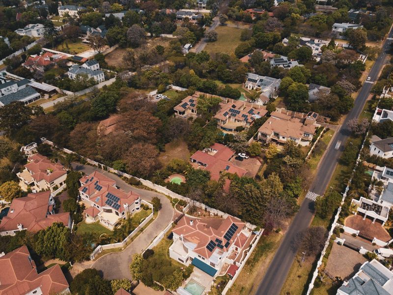 An aerial view of a residential neighborhood featuring established homes, mature trees, paved streets, and private swimming pools.