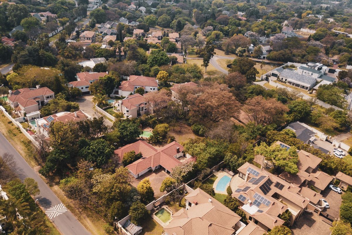 An aerial view of a well-established residential neighborhood featuring multiple homes with tiled roofs, swimming pools, and mature landscaping.