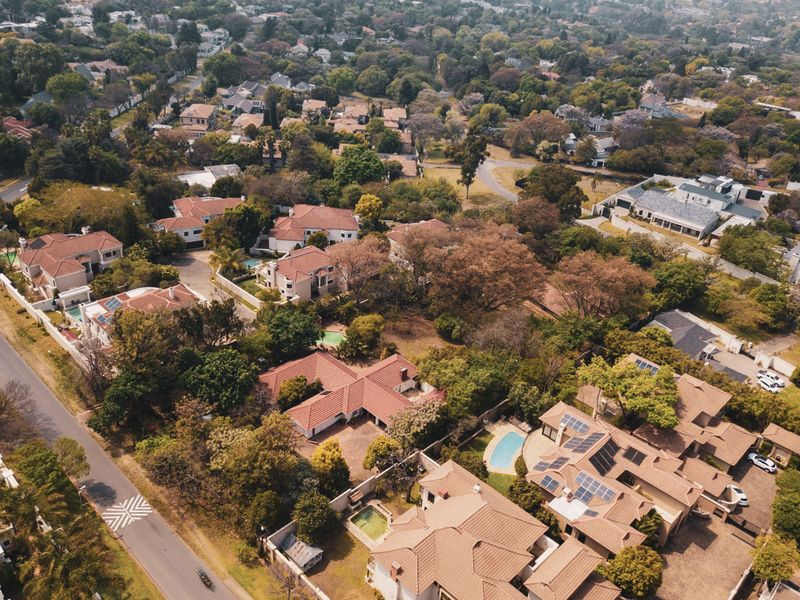 An aerial view of a well-established residential neighborhood featuring multiple homes with tiled roofs, swimming pools, and mature landscaping.
