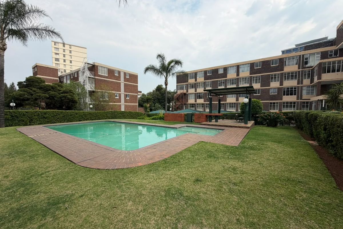 Communal outdoor area featuring a swimming pool, brick paving, a pergola, and well-maintained garden space within the apartment complex.