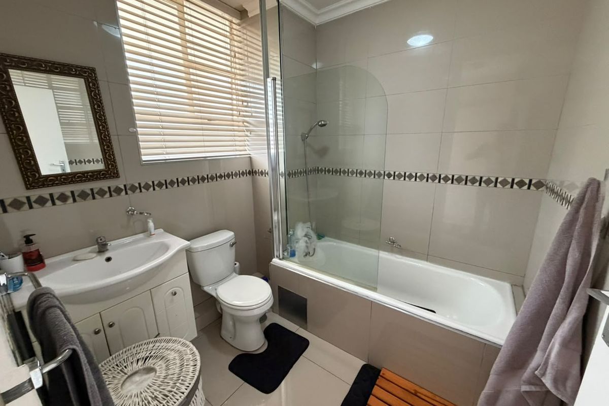 A functional bathroom featuring a vanity cabinet, toilet, and a bathtub with a glass shower screen, finished with neutral wall and floor tiles.
