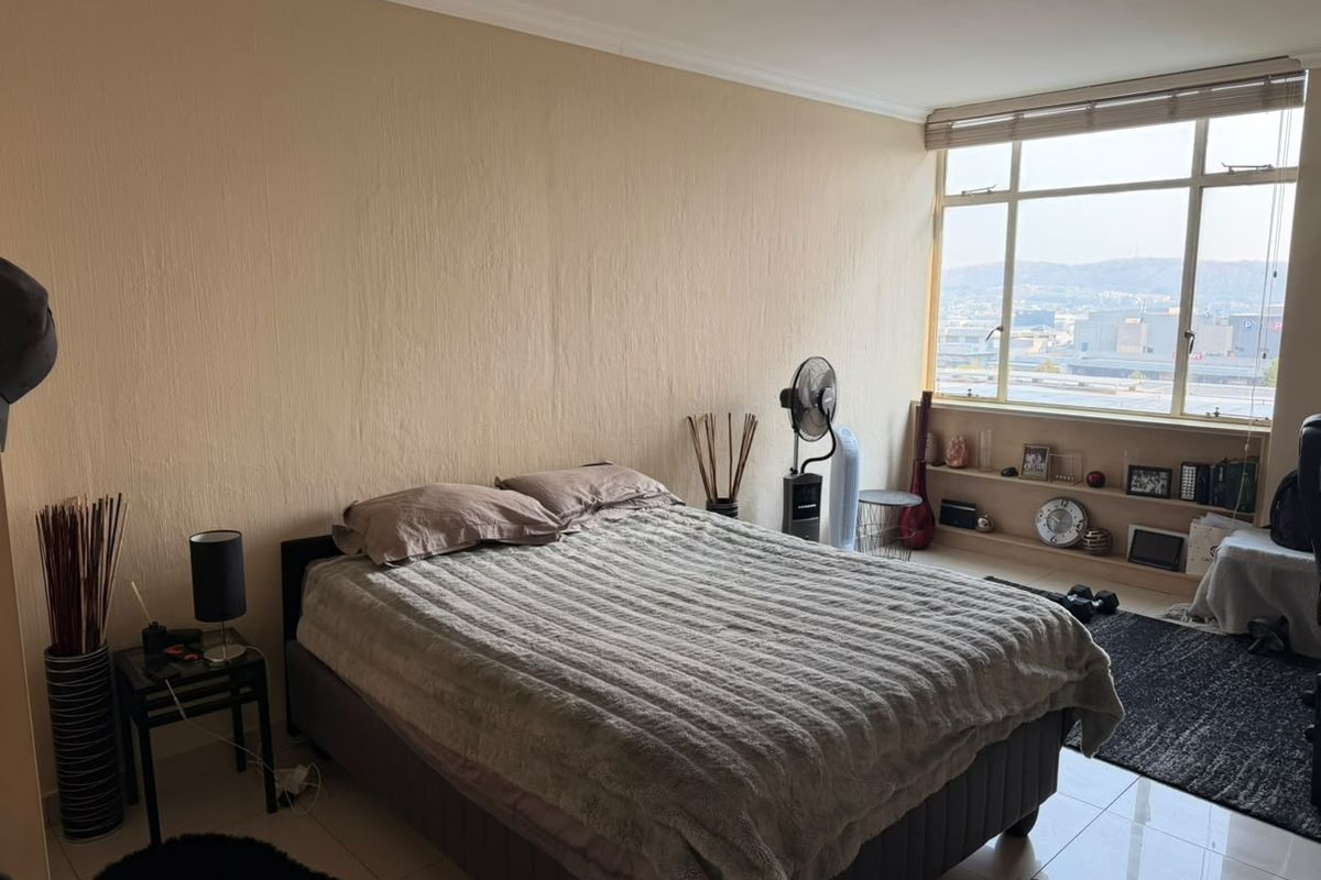 A bedroom featuring large windows with city views, built-in shelving, and tiled flooring, offering a bright and functional living space.