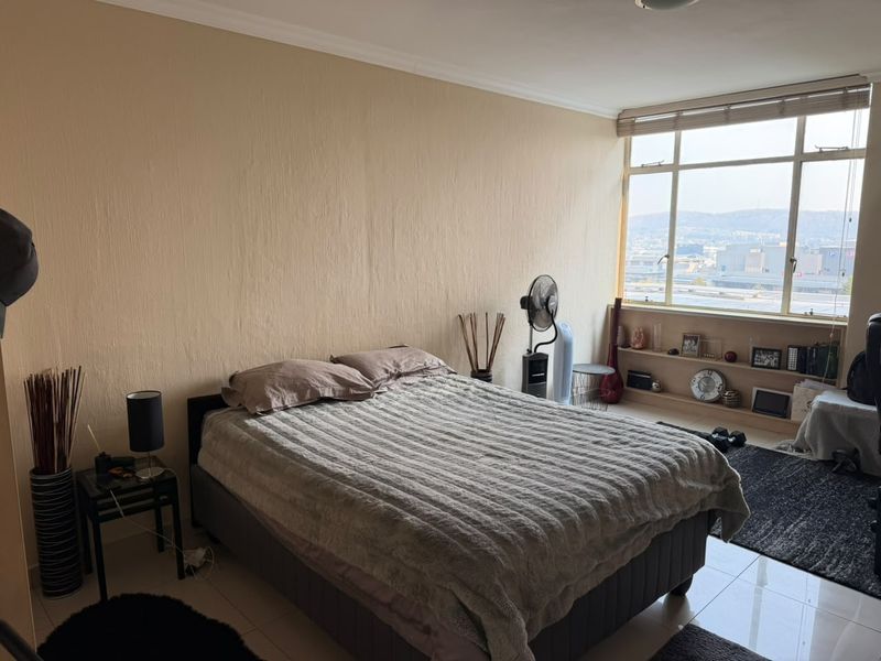 A bedroom featuring large windows with city views, built-in shelving, and tiled flooring, offering a bright and functional living space.