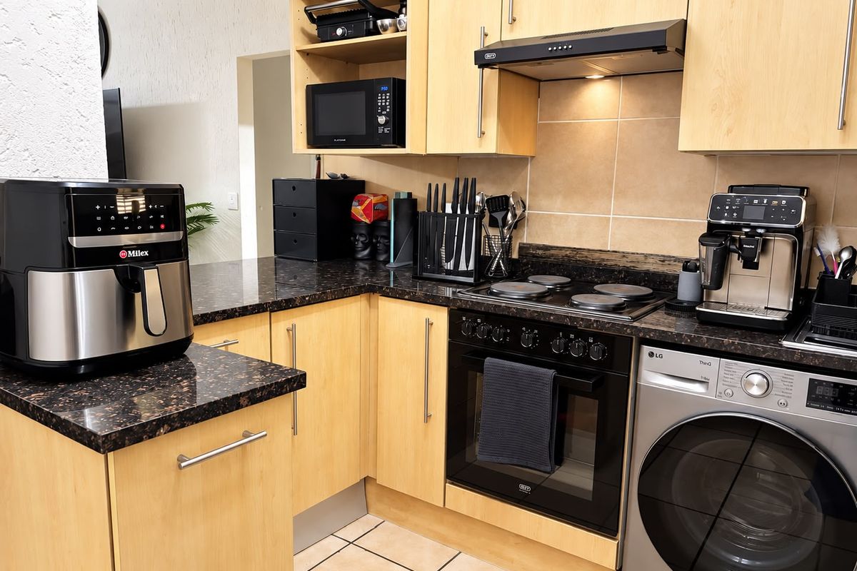 A functional kitchen featuring light wood cabinetry, dark granite countertops, a built-in oven with hob, and an integrated washing machine.