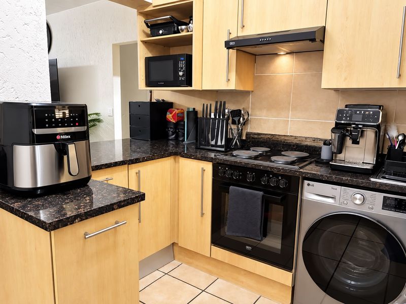 A functional kitchen featuring light wood cabinetry, dark granite countertops, a built-in oven with hob, and an integrated washing machine.