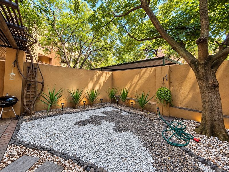 A well-maintained private garden area featuring decorative stone landscaping, perimeter walls, mature trees, and integrated low-voltage garden lighting.