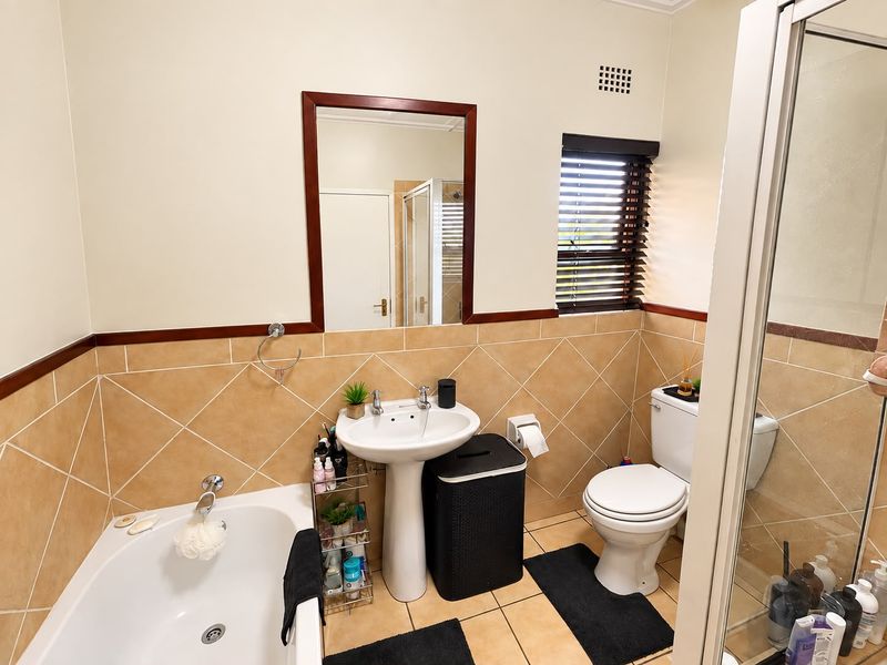 A functional bathroom featuring a pedestal sink, bathtub, separate shower enclosure, and neutral ceramic tiling throughout.
