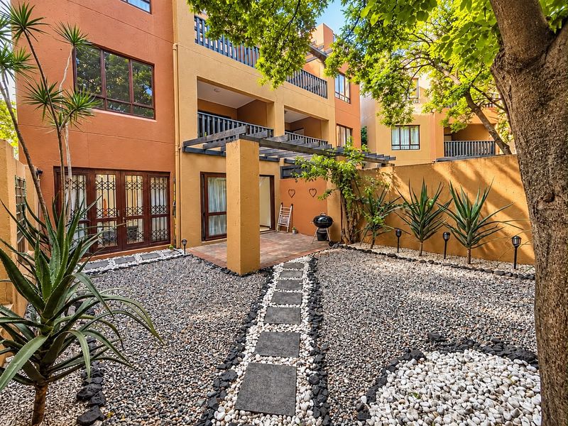 A well-maintained rear courtyard featuring a paved patio area, timber pergola, and landscaped garden with stone pathways and pebble beds.