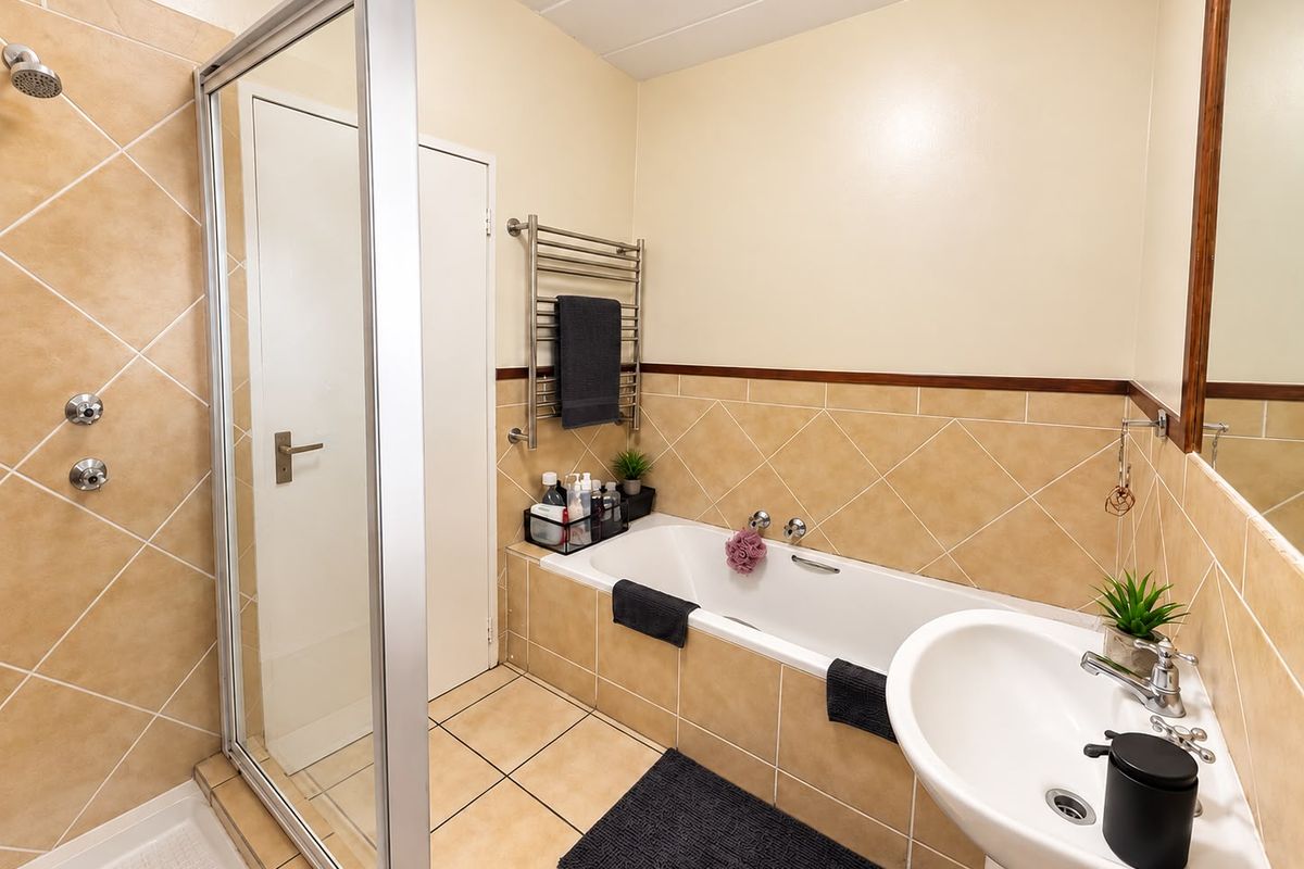 A functional bathroom featuring a shower enclosure, bathtub, pedestal sink, and a heated towel rail with neutral tiled finishes.