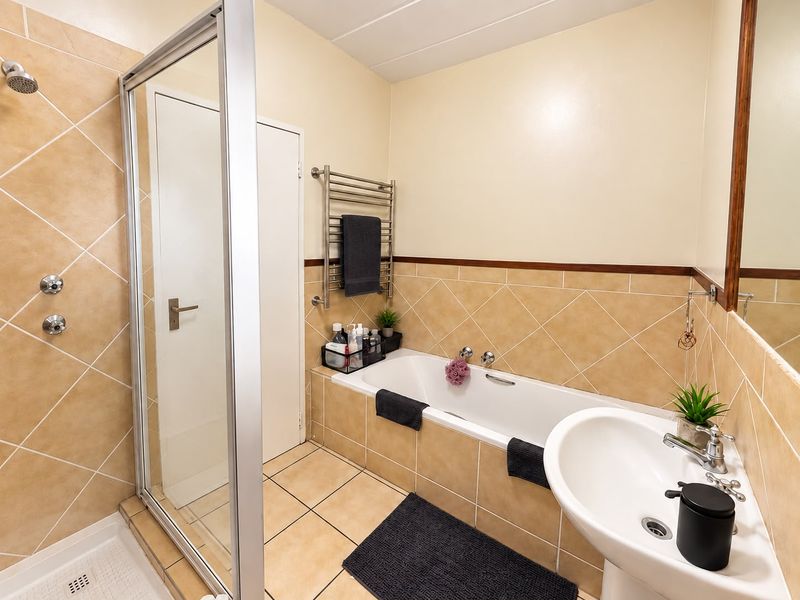 A functional bathroom featuring a shower enclosure, bathtub, pedestal sink, and a heated towel rail with neutral tiled finishes.
