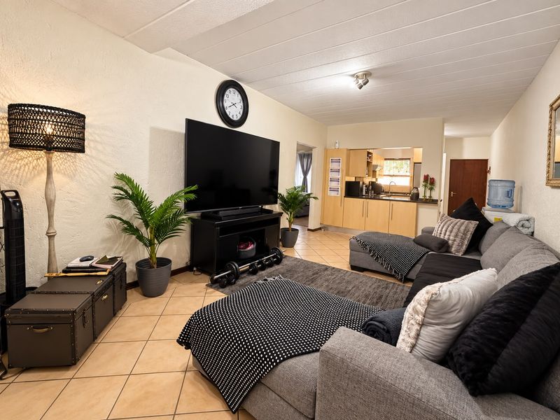 Open-plan living area featuring tiled flooring and a connected kitchen with light wood cabinetry and functional workspace.