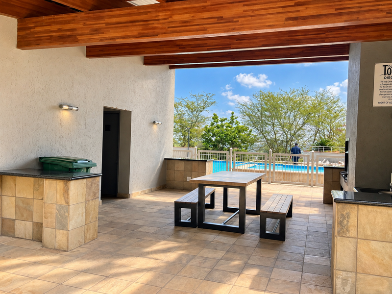 Covered outdoor patio featuring exposed timber beams, built-in stone-clad counters with granite tops, and direct access to the swimming pool area.