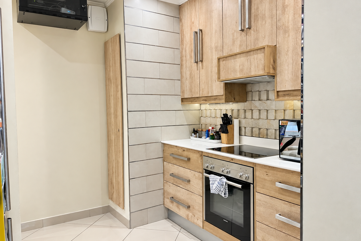Modern kitchen featuring light wood-finish cabinetry, integrated oven and hob, stone countertops, and a stylish tiled backsplash.