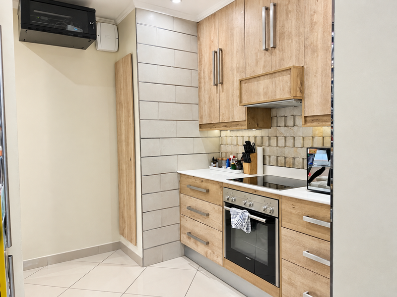 Modern kitchen featuring light wood-finish cabinetry, integrated oven and hob, stone countertops, and a stylish tiled backsplash.