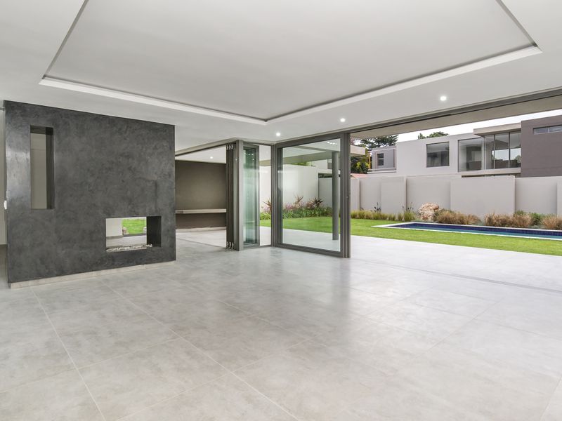 Spacious open-plan living area featuring large format tiles, a modern built-in fireplace, and seamless indoor-outdoor flow through stacking doors to the pool and garden.