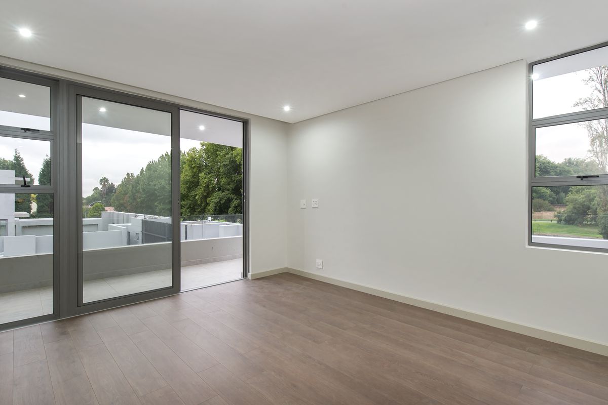 A bright, modern, and empty bedroom featuring laminate flooring, recessed downlights, and large aluminium sliding doors leading to a private balcony.