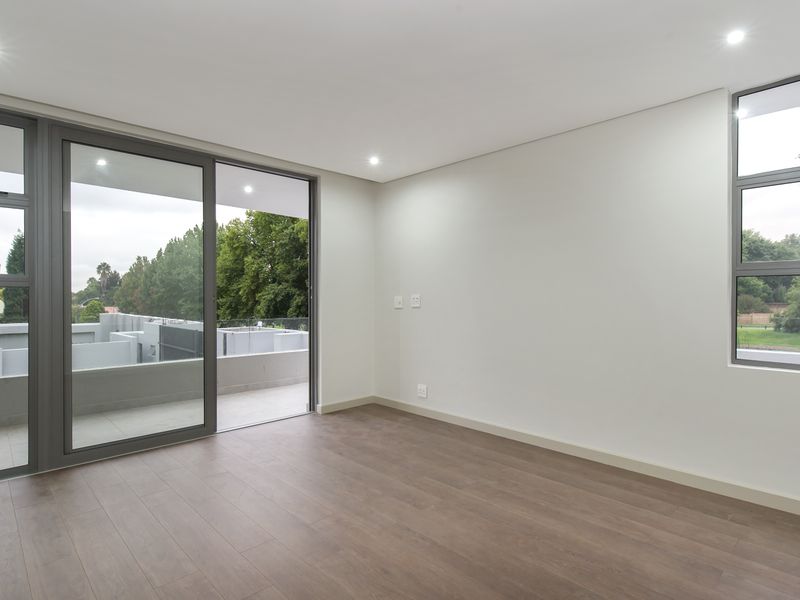 A bright, modern, and empty bedroom featuring laminate flooring, recessed downlights, and large aluminium sliding doors leading to a private balcony.
