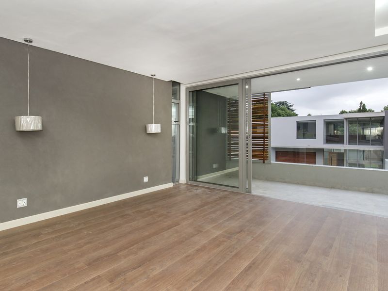 Spacious, modern living area featuring laminate flooring, recessed lighting, and large sliding glass doors opening onto a private balcony.