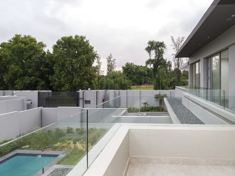 Modern elevated balcony featuring a sleek glass balustrade, overlooking a private swimming pool and landscaped garden area within a secure cluster property.