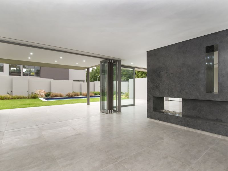 Spacious open-plan living area featuring large bi-fold doors opening to a garden and pool, complemented by a modern built-in fireplace and tiled flooring.