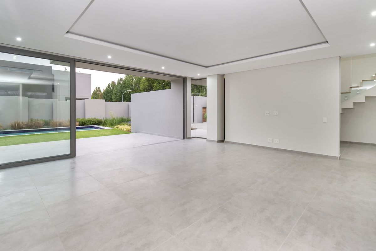 Spacious, modern open-plan living area featuring large sliding glass doors that open to a private garden and pool, with a sleek floating staircase.