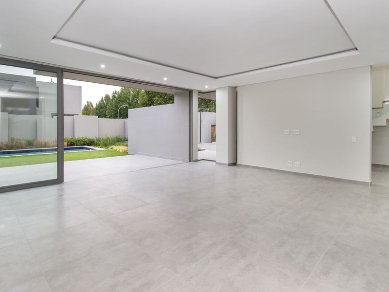 Spacious, modern open-plan living area featuring large sliding glass doors that open to a private garden and pool, with a sleek floating staircase.