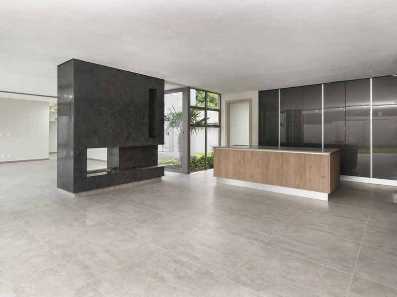 Spacious open-plan living area featuring a modern built-in fireplace, sleek kitchen island, and high-gloss cabinetry with large format floor tiles.