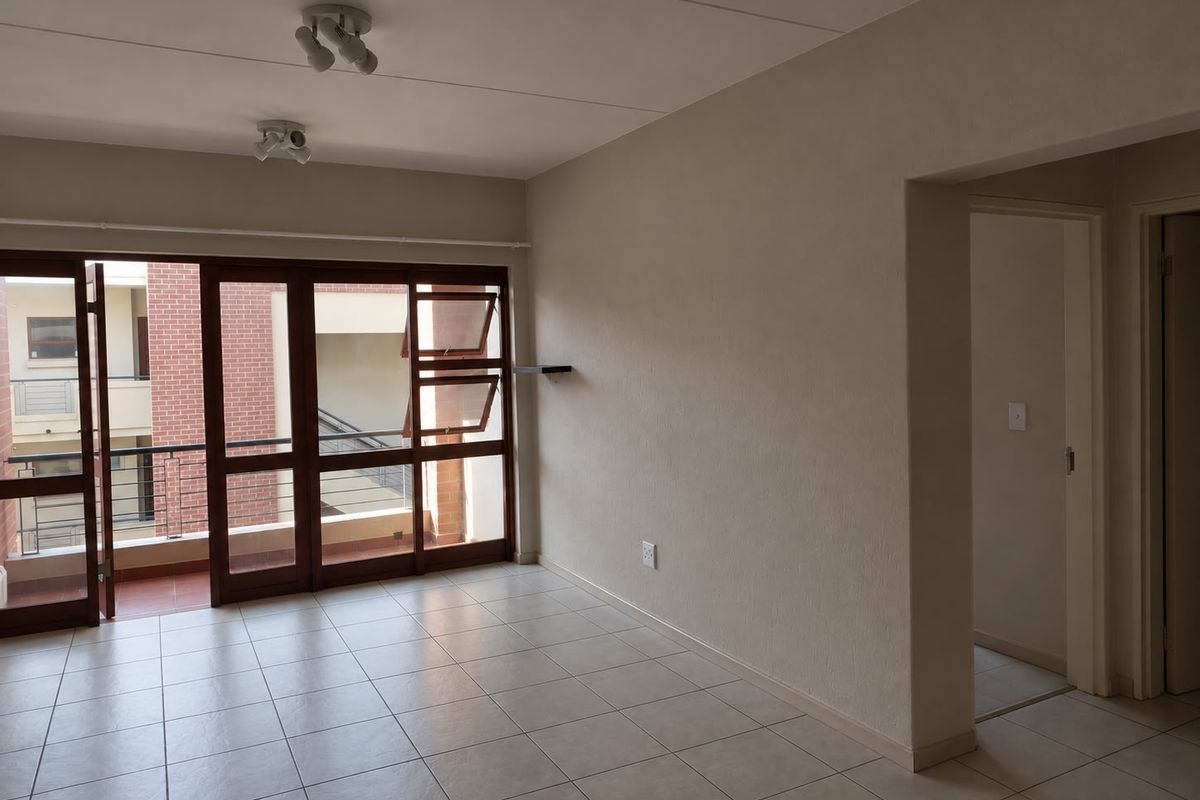 An empty, neutrally painted living room featuring tiled flooring, ceiling spotlights, and a large sliding glass door providing access to an outdoor balcony.