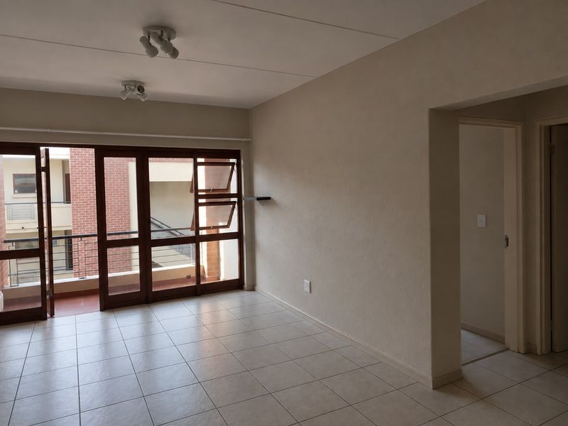 An empty, neutrally painted living room featuring tiled flooring, ceiling spotlights, and a large sliding glass door providing access to an outdoor balcony.
