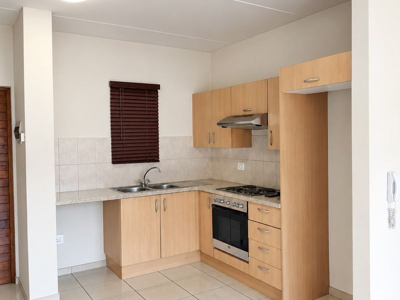 A clean, functional kitchen featuring light wood cabinetry, granite-look countertops, built-in oven and hob, and neutral tiled flooring.