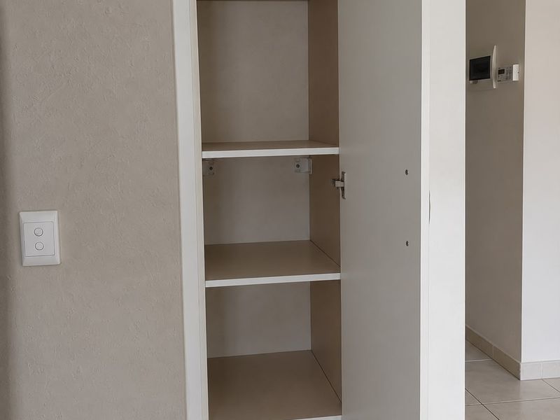 A clean, built-in storage cupboard with multiple shelves, located in a tiled apartment hallway.