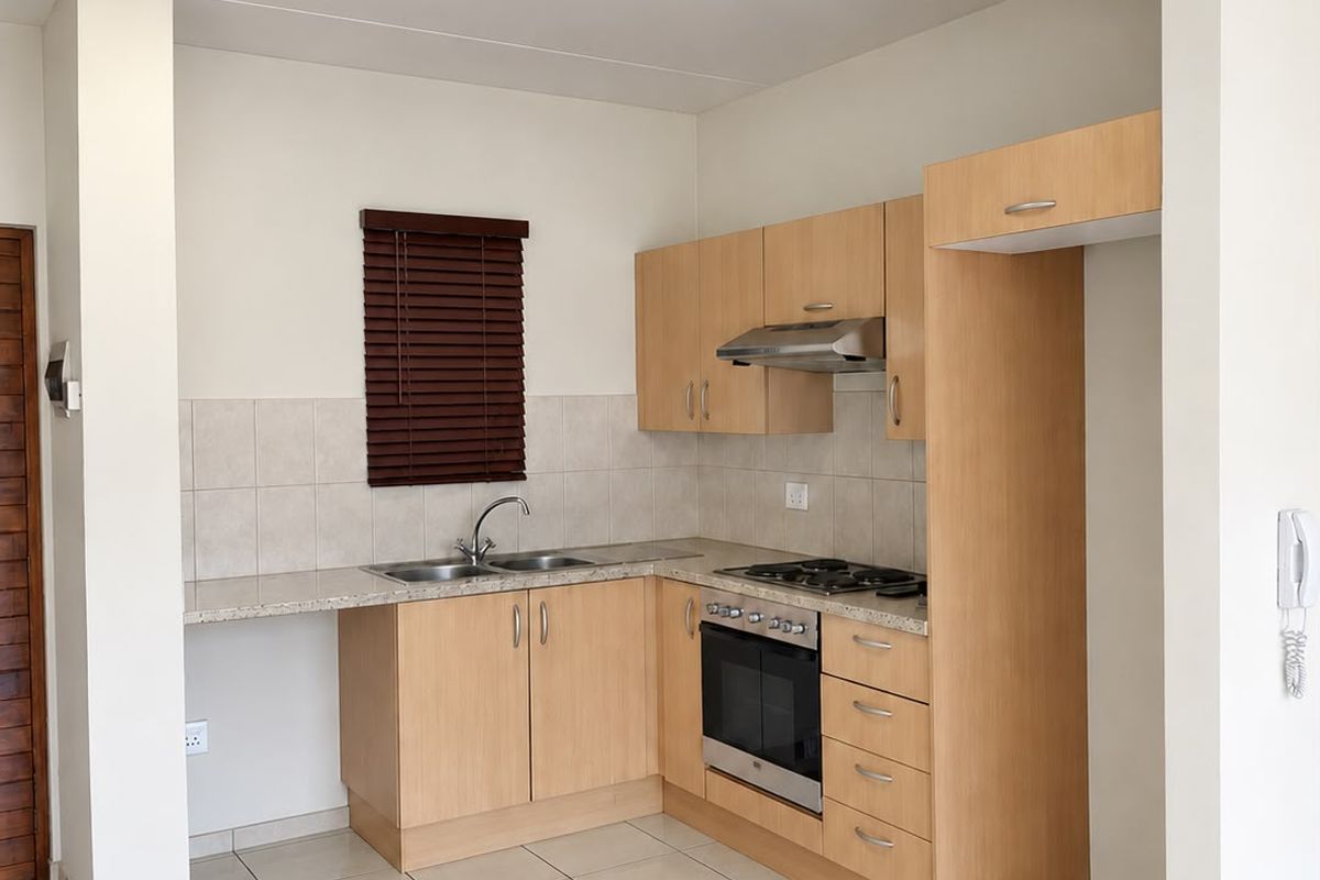 A clean, functional kitchen featuring light wood cabinetry, granite-look countertops, built-in oven and hob, and neutral tiled flooring.
