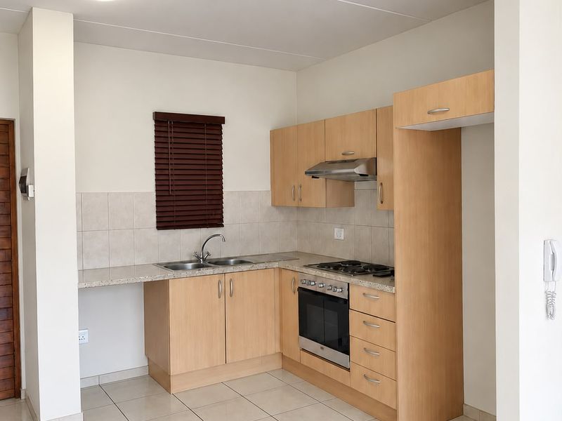 A clean, functional kitchen featuring light wood cabinetry, granite-look countertops, built-in oven and hob, and neutral tiled flooring.